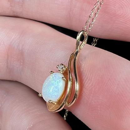 Side close-up view of Coober Pedy, Australian opal and diamond pendant in 14k gold with chain, held in hand