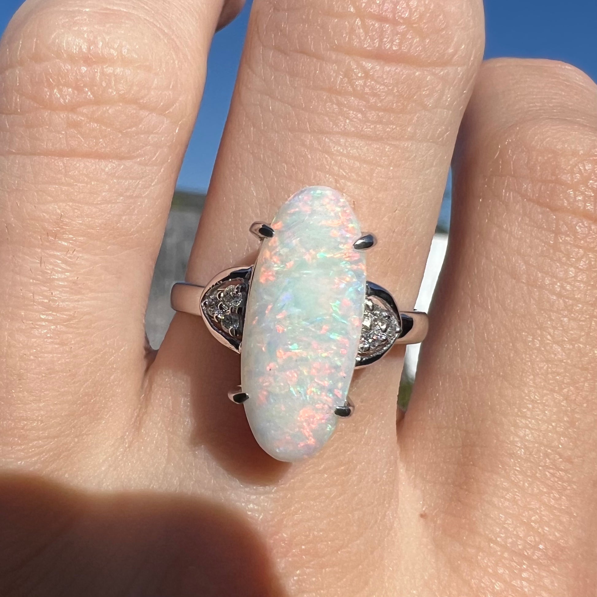 A Coober Pedy white opal platinum ring set with diamond accents.  The opal plays soft pink colors.