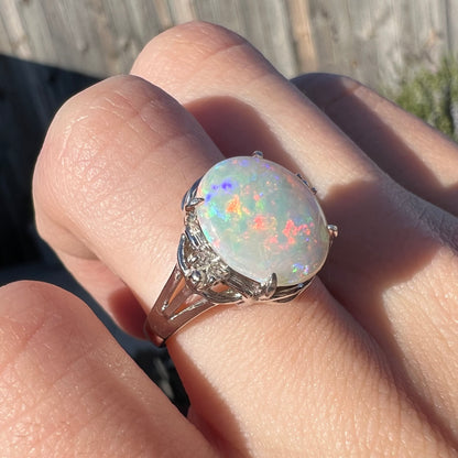 A platinum Coober Pedy opal and diamond ring with red and purple colors worn on a hand in the sunlight.