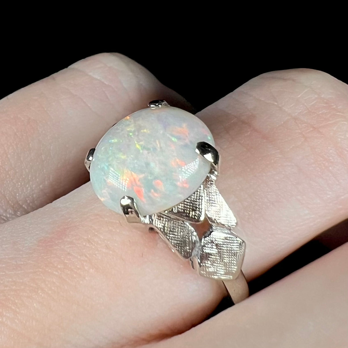 A textured 14k white gold women's ring set with a Coober Pedy, Australian opal, worn on a finger and shown close-up from an angle