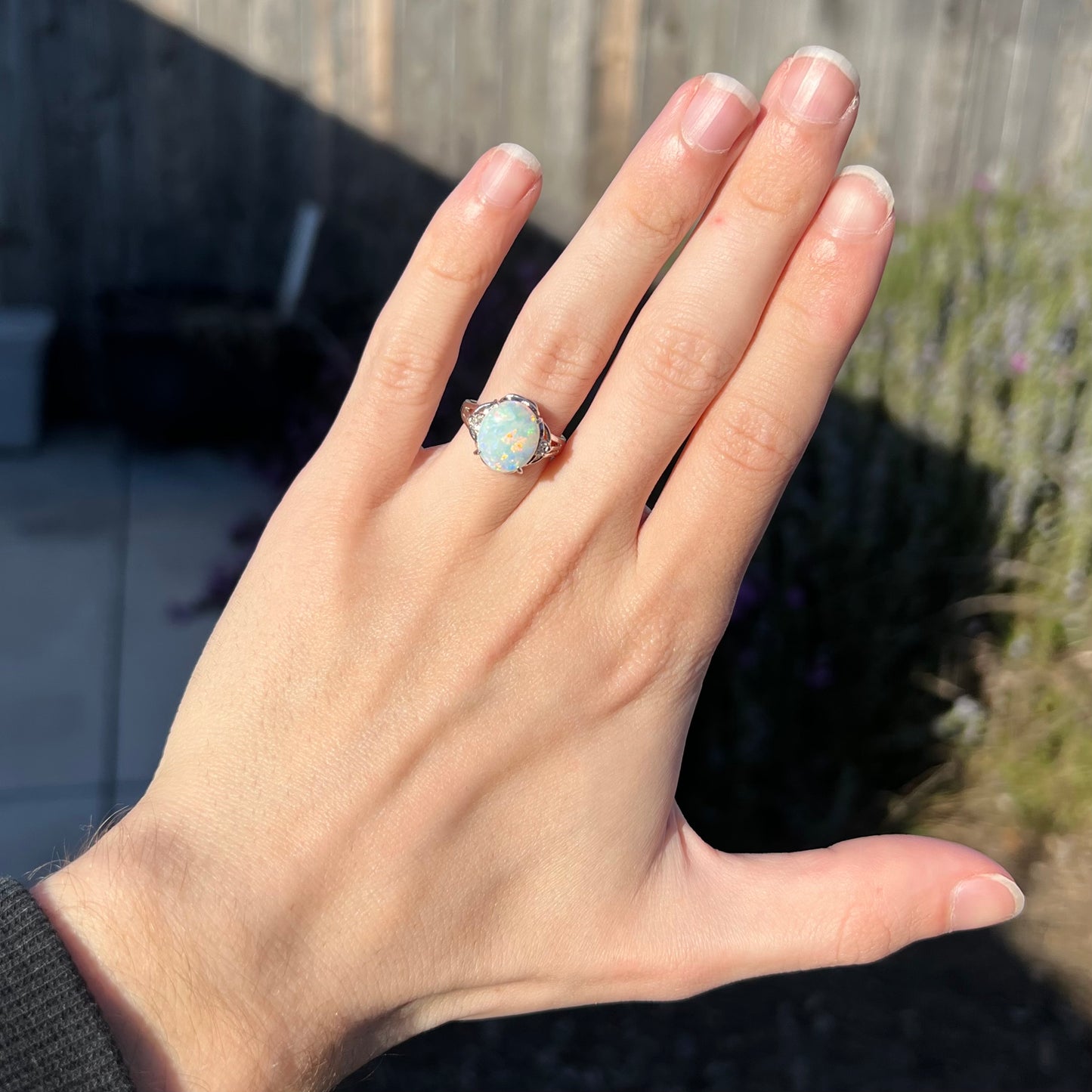 A platinum Coober Pedy opal and diamond ring, worn on a hand in the sunlight.