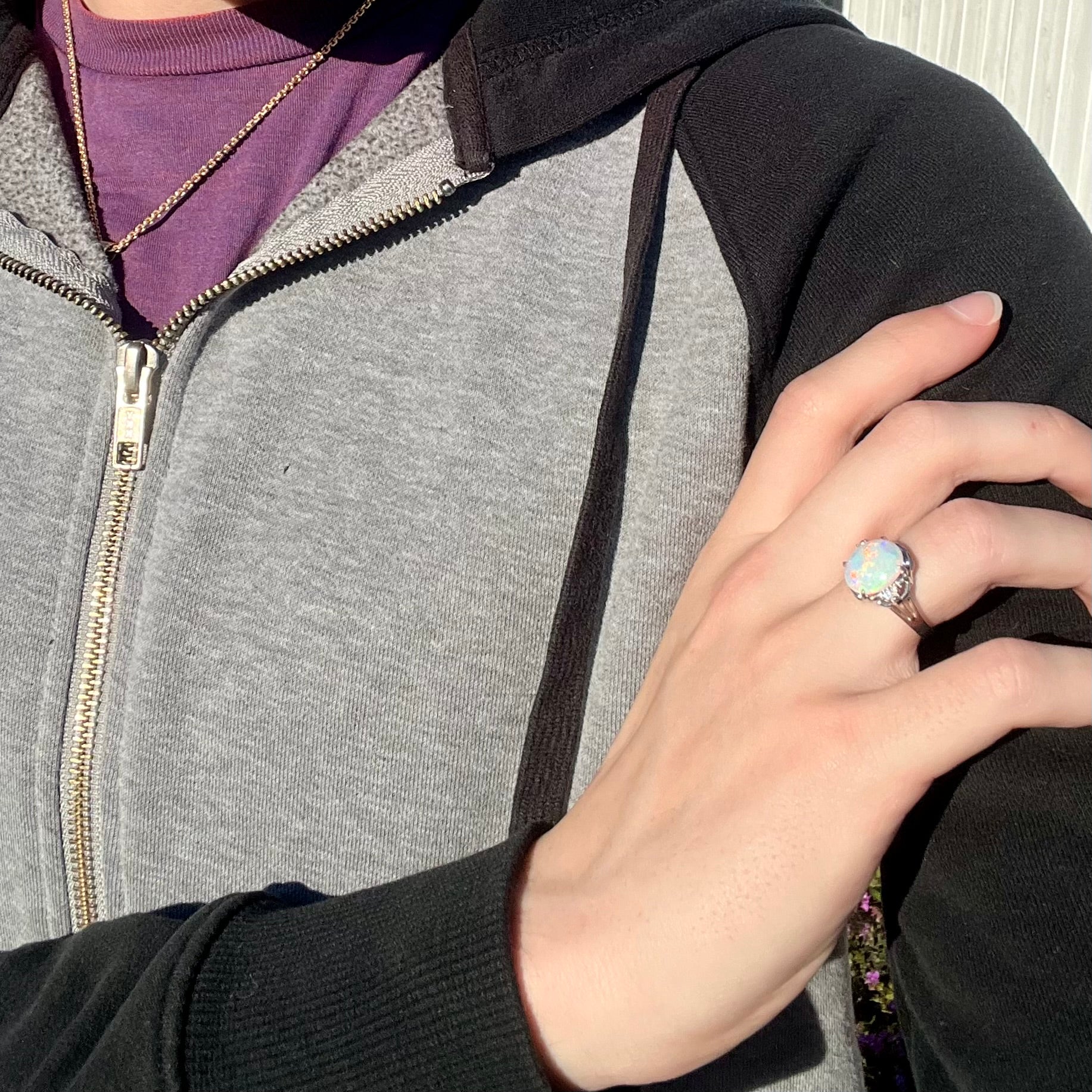 A platinum Coober Pedy opal ring with diamond accents, worn on a model's hand in the sunlight.