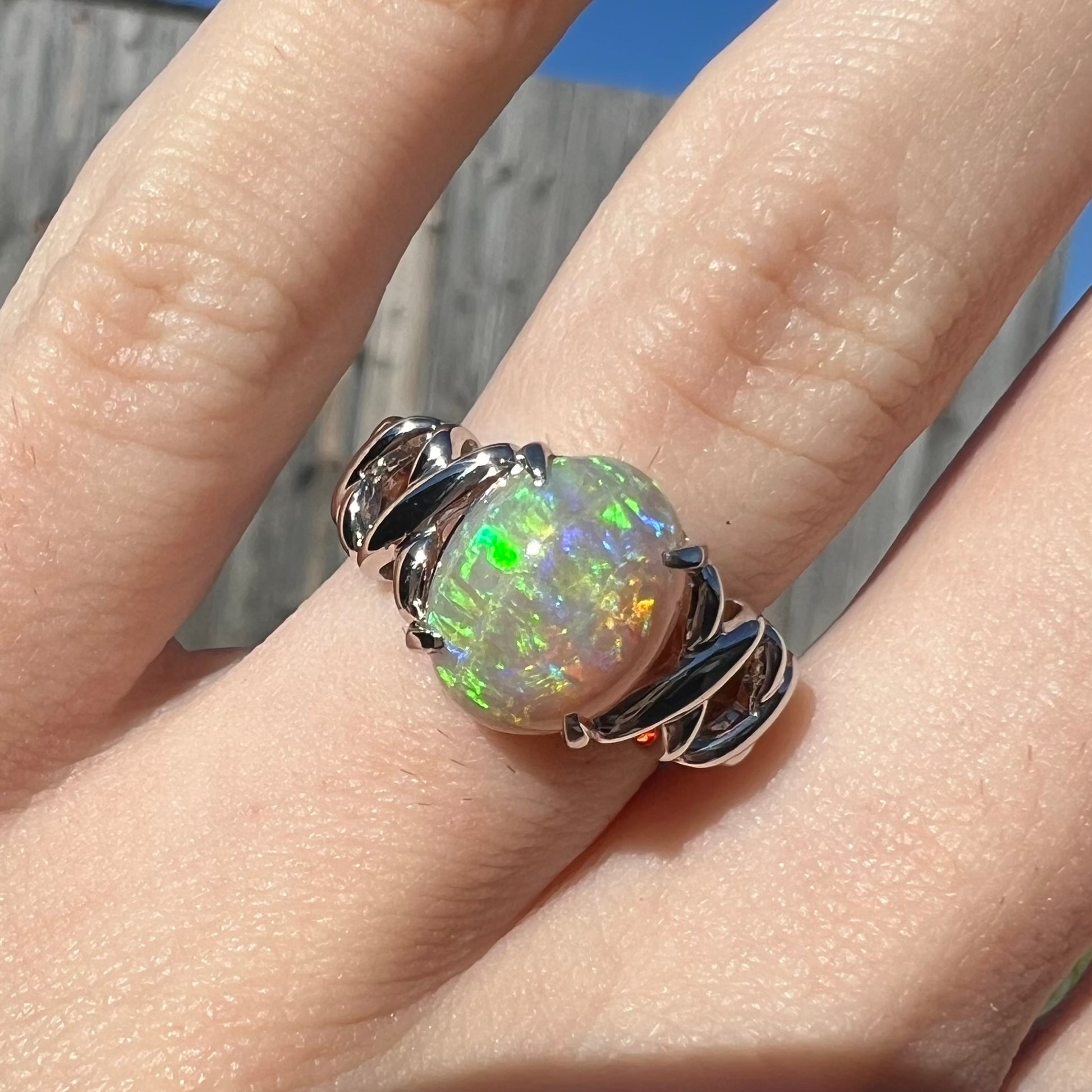 A 2.20ct Coober Pedy opal ring worn on a finger in the sunlight.  The ring has platinum crisscross designs.