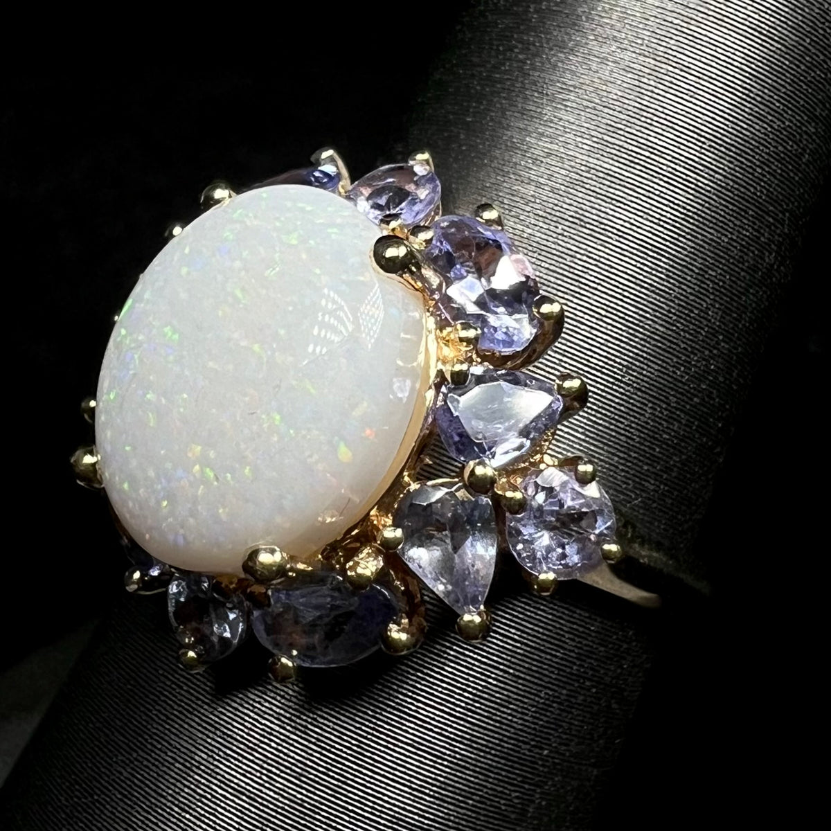 Angled close-up of white Coober Pedy, Australian opal and tanzanite-accented ring, shown on ring display