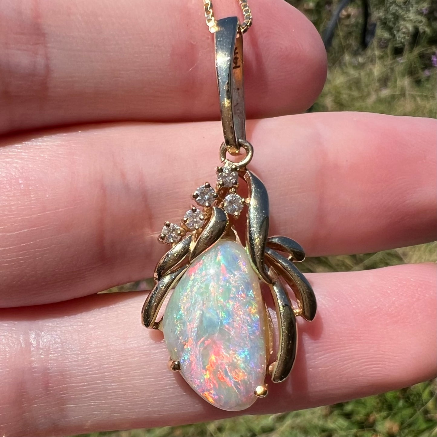 Close-up of a Coober Pedy shell opal pendant in 14k gold with diamond accents, viewed in the sunlight.  Multicolor fire and crazing are seen in the opal.