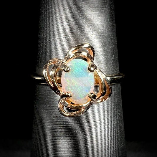 A yellow gold ring mounted with an oval cut opal.  The opal has a white base tone with green and blue color play.