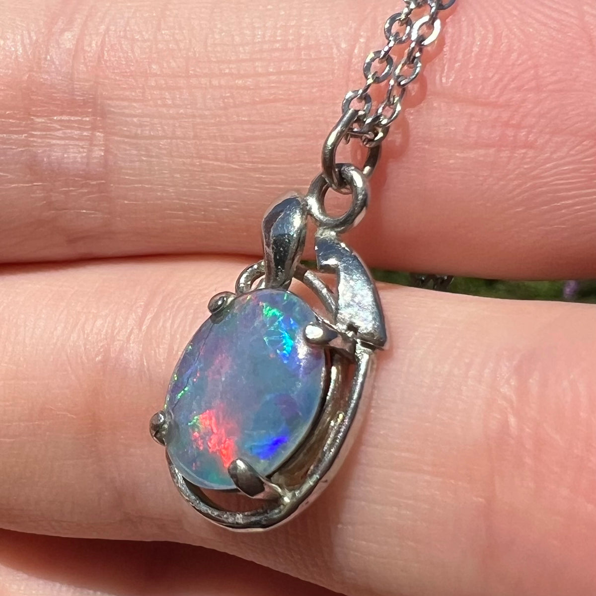 Costume opal triplet necklace shown close-up in hand from angle under sunlight