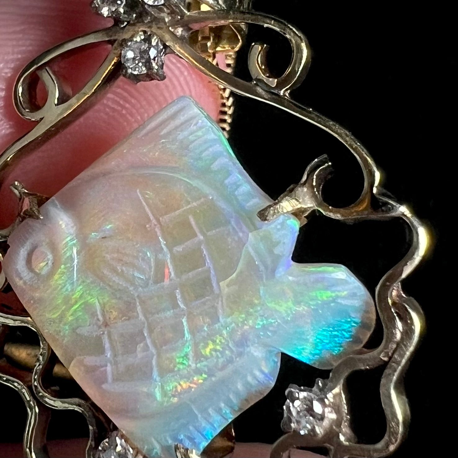 Macro close-up of crack beneath prong in carved Australian opal fish, mounted with diamonds in gold pendant