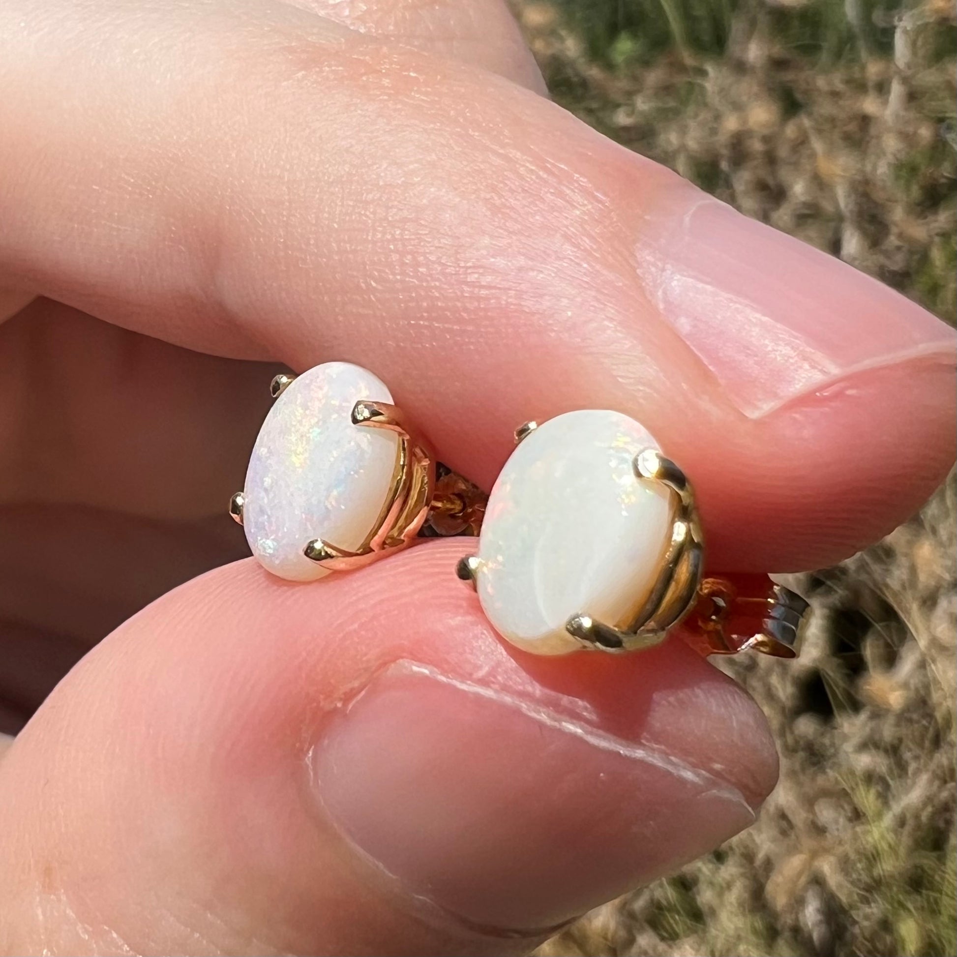 Crazed Australian opal stud earrings in sunlight, shown from angle between two fingers