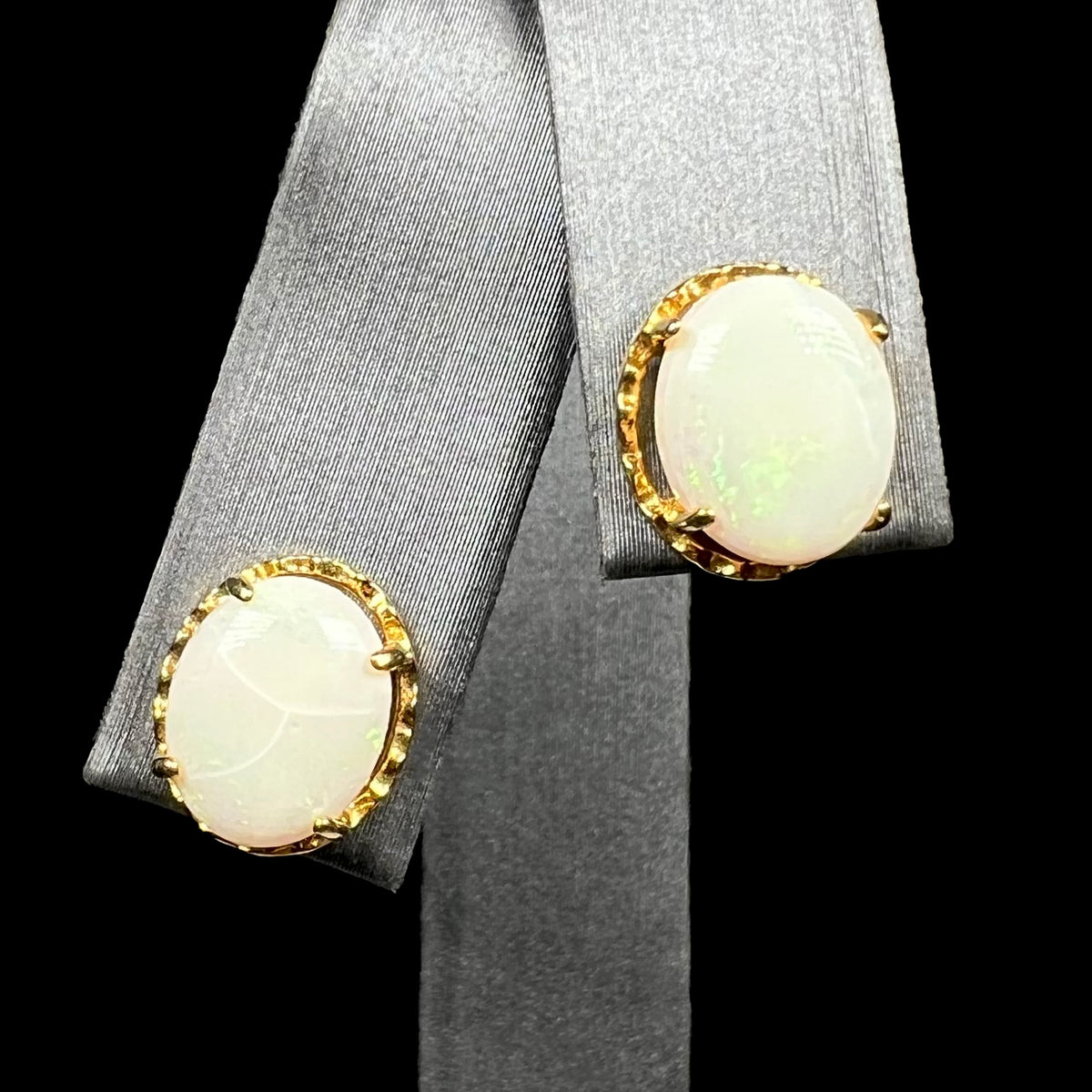 Pair of gold-tone stud earrings set with crazed white Australian opals, shown on earring display