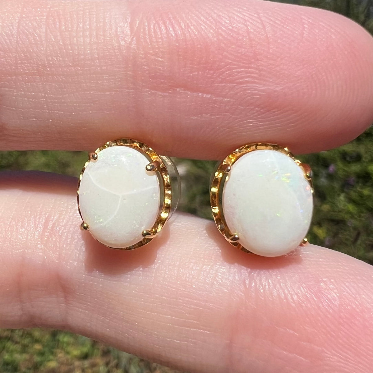 Close-up of crazed Australian opal stud earrings in gold-plated base metal, shown between fingers in sunlight