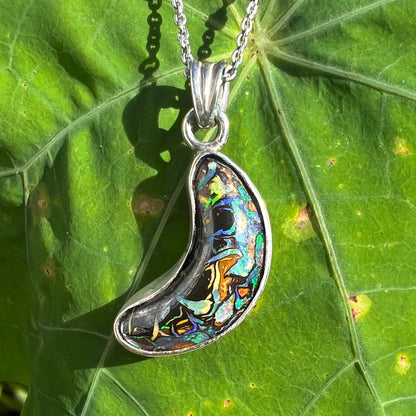 A sterling silver necklace set with a natural Koroit boulder opal shaped like a crescent moon.