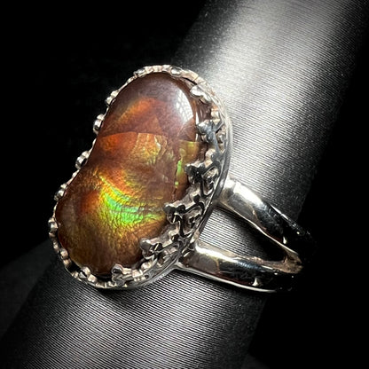 A fire agate ring with silver crown-design prongs shown at an angled view against black backdrop.