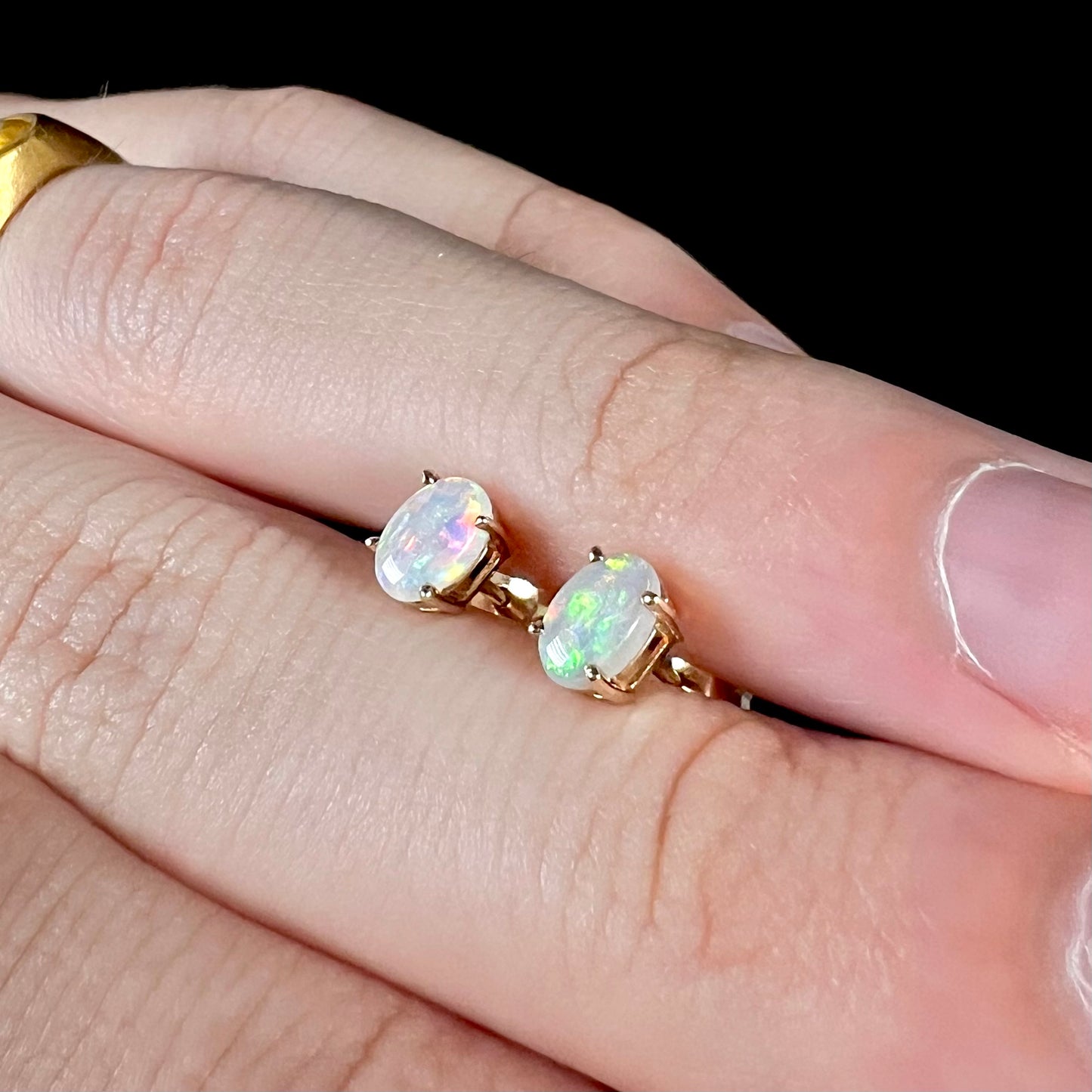 Opal stud earrings viewed at an opposing angle, one opal appearing green and the other purple.