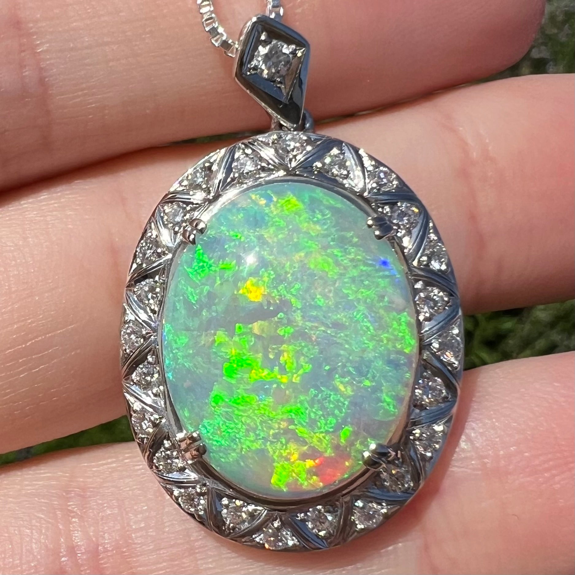 Macro close-up of opal pendant in sunlight showing intense green flash with red, blue, and yellow sparks.
