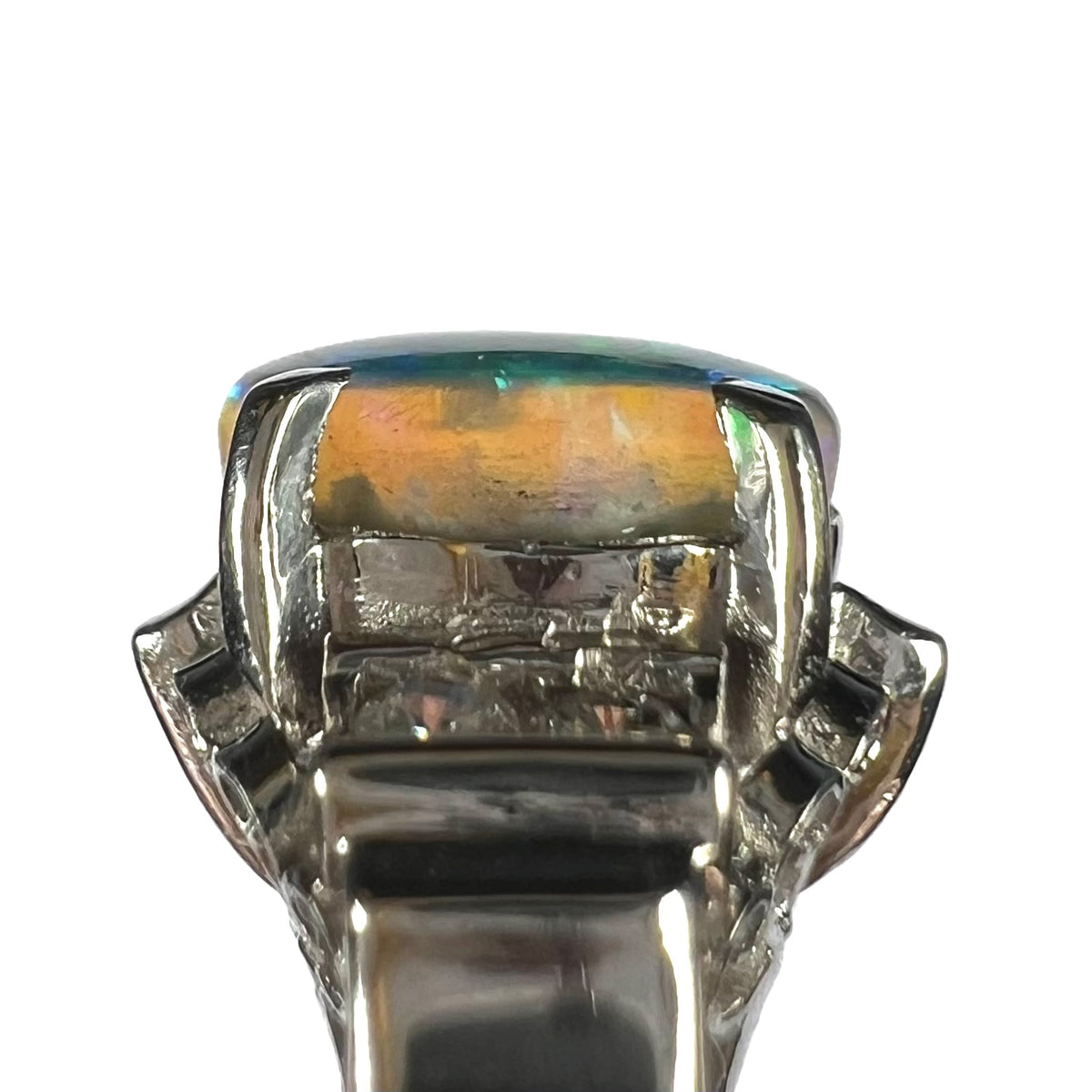 Side view of Australian black opal in prong-set ring showing irregular natural matrix extending into the crystal opal, shown against white background.