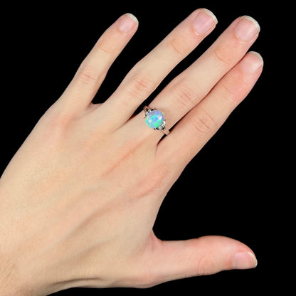 A Lightning Ridge crystal opal ring on a hand.  The ring is platinum with diamond accents.