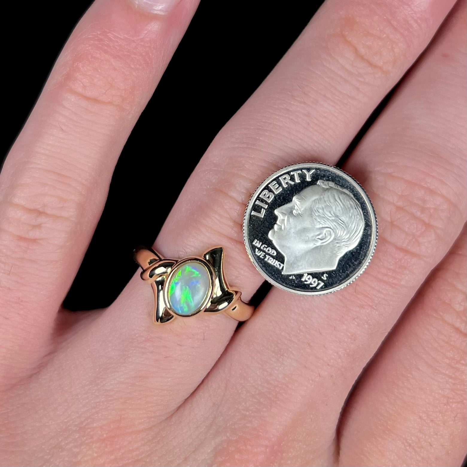 A delicate, yellow gold crystal opal ring worn on a hand next to a US dime coin.