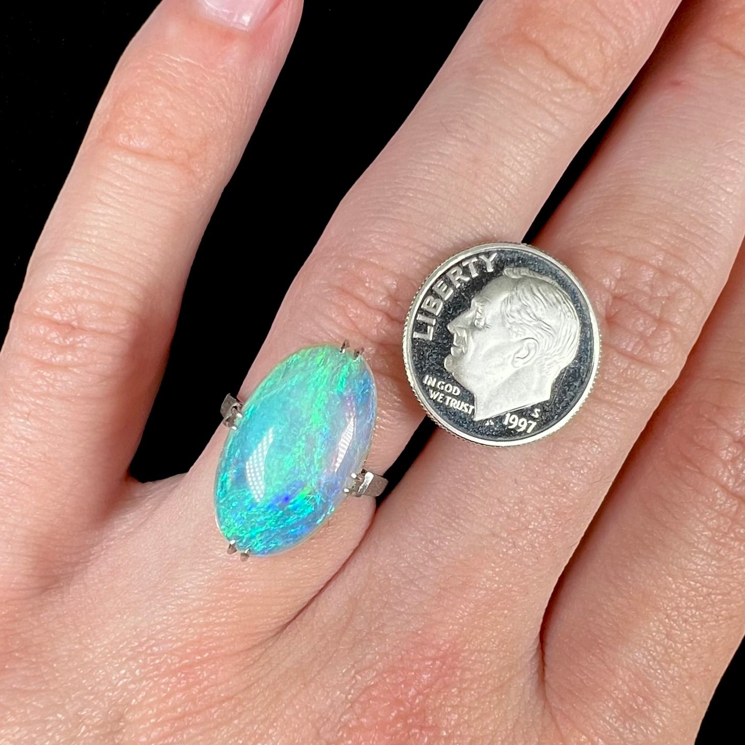 A platinum crystal opal ring worn on a hand next to a US dime coin.