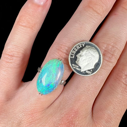 A platinum crystal opal ring worn on a hand next to a US dime coin.