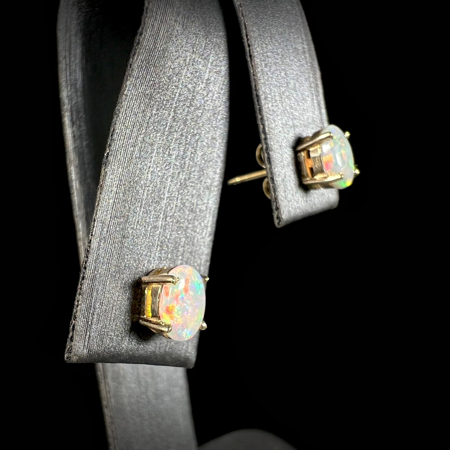 A close-up of crystal opal earrings in 14k gold, showing a red fire flash.