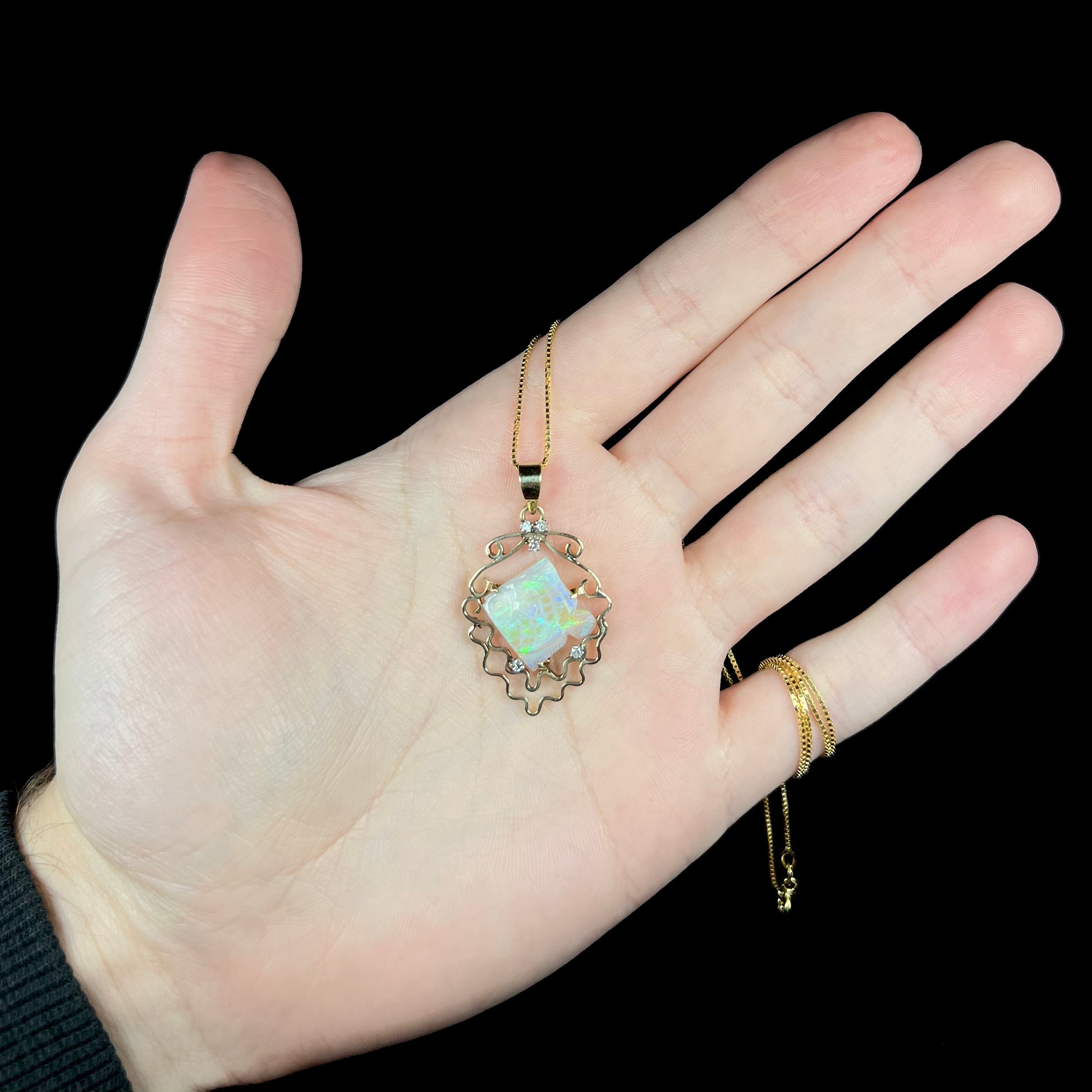 Hand holding custom-made 14k yellow gold opal fish necklace with diamond accents