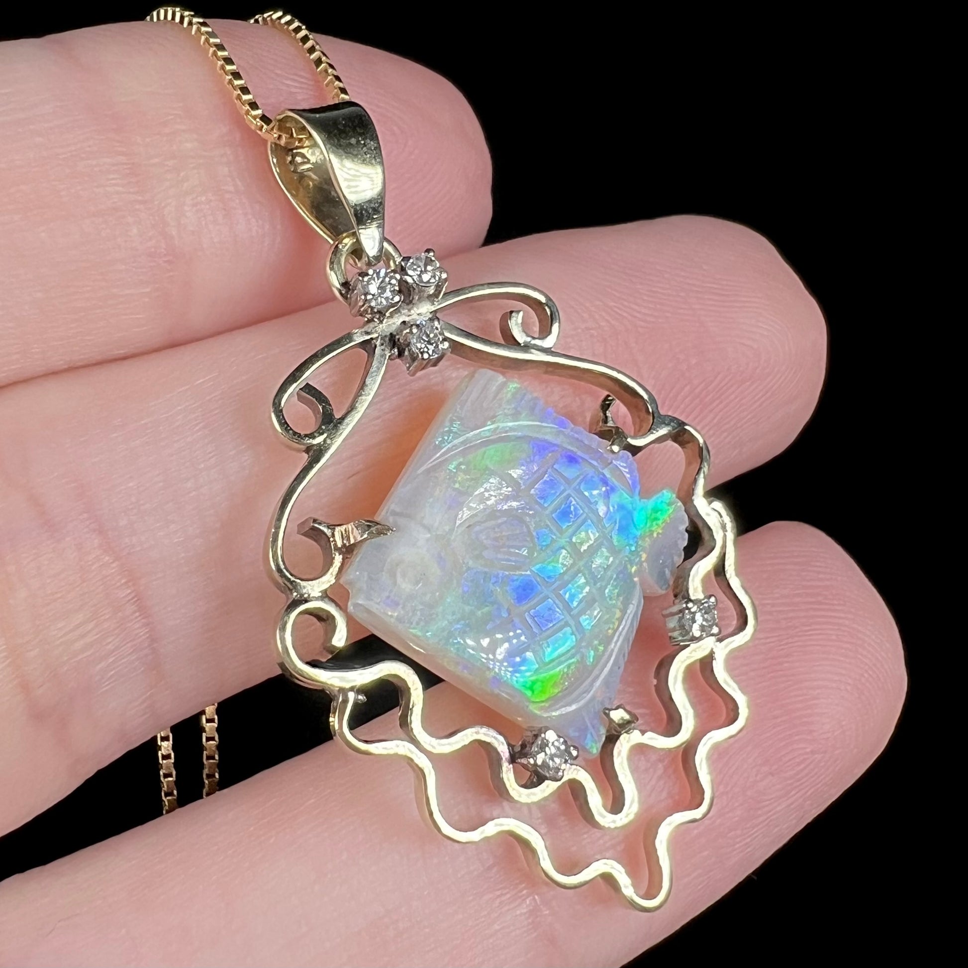 Custom made opal and diamond fish pendant in 14k gold, shown close-up in hand