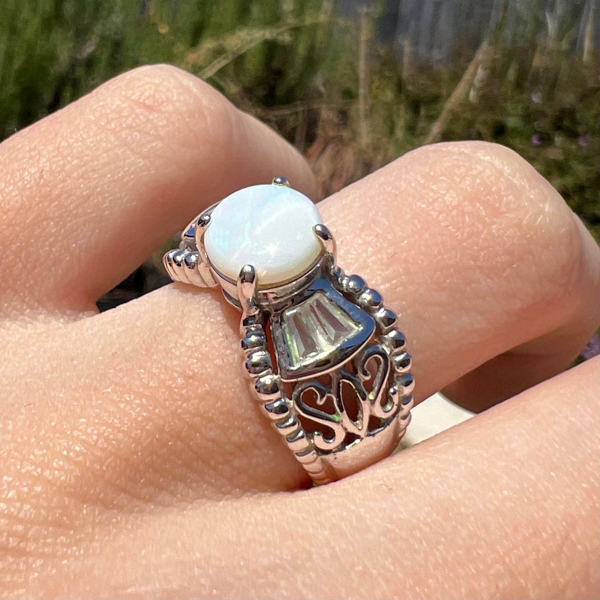 Close-up angled sunlit view of a round Australian white opal and CZ ring in white base metal. 