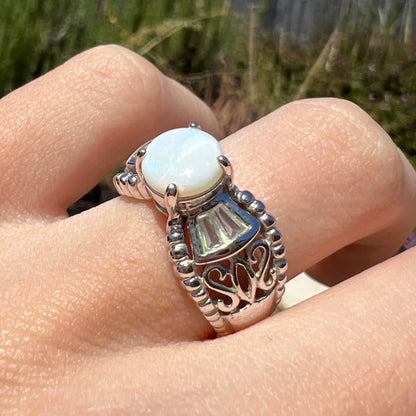 Close-up angled sunlit view of a round Australian white opal and CZ ring in white base metal. 