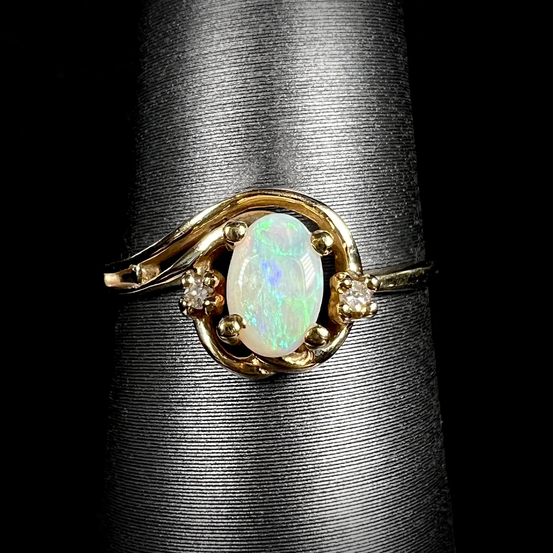 A dainty 10k yellow gold Australian opal and diamond engagement ring with asymmetrical split-shank design shown close-up on ring display.