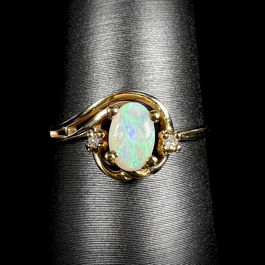 A dainty 10k yellow gold Australian opal and diamond engagement ring with asymmetrical split-shank design shown close-up on ring display.