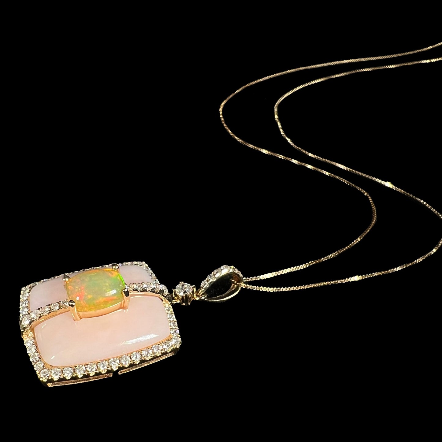 A dainty 14k gold Ethiopian fire opal, pink Peruvian opal, and diamond pave necklace by Cirari laying on a black background, its gold chain flowing.