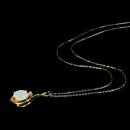 Dainty 14k gold women's opal and diamond necklace shown from angle laying on black background, the chain flowing behind the pendant