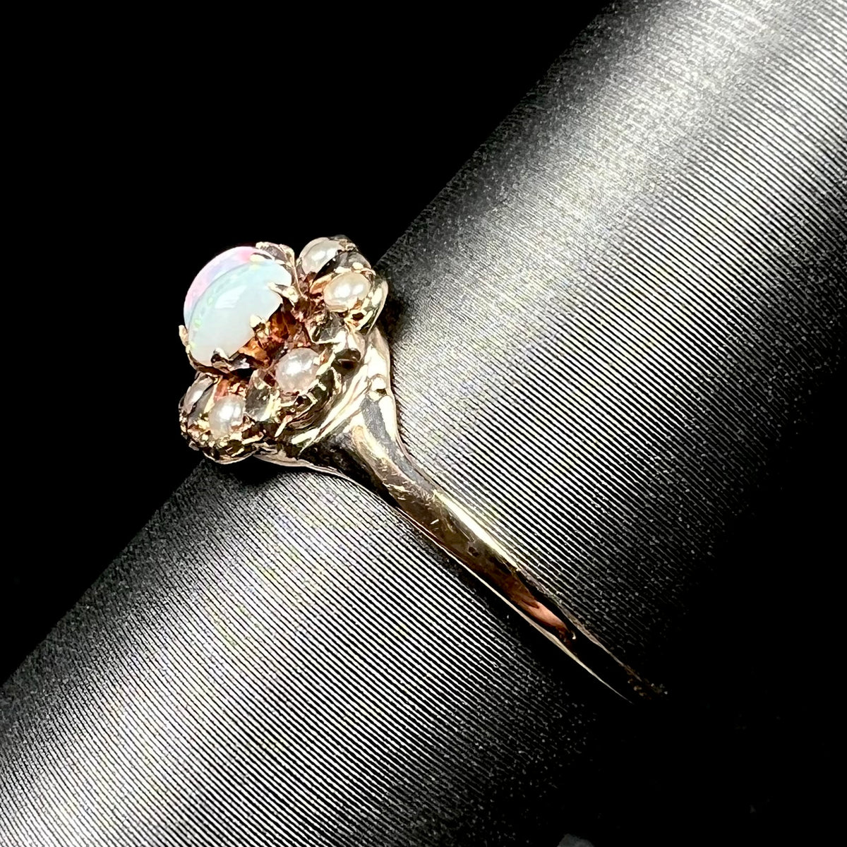 Side view of a Victorian 9k gold opal and pearl ring on a ring display, the ring's dainty gold shank in focus