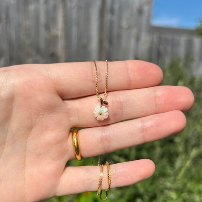 Hand holding a dainty Australian white opal flower pendant on a box chain in natural sunlight against blurred outdoor background.
