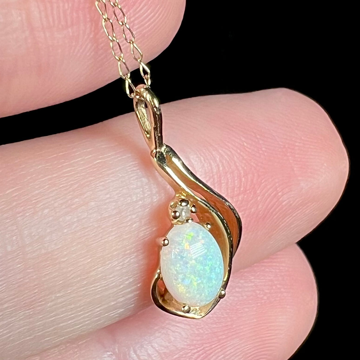 Angled macro view of dainty Australian opal pendant with diamond accent, held in hand