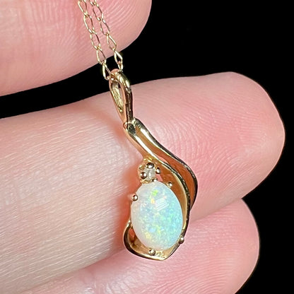 Angled macro view of dainty Australian opal pendant with diamond accent, held in hand
