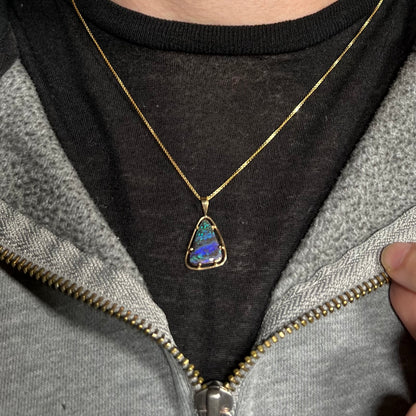 A dainty Duck Creek opalized wood necklace in 9k gold worn around a neck against a dark shirt.