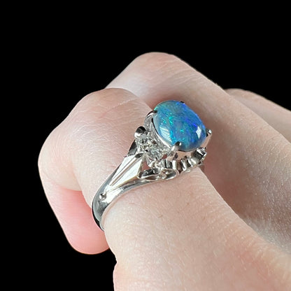 A dainty black opal ring set in platinum with diamond accents on a finger.