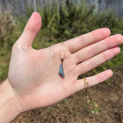 Hand holding dainty 18k gold boulder opal pendant in sunlight
