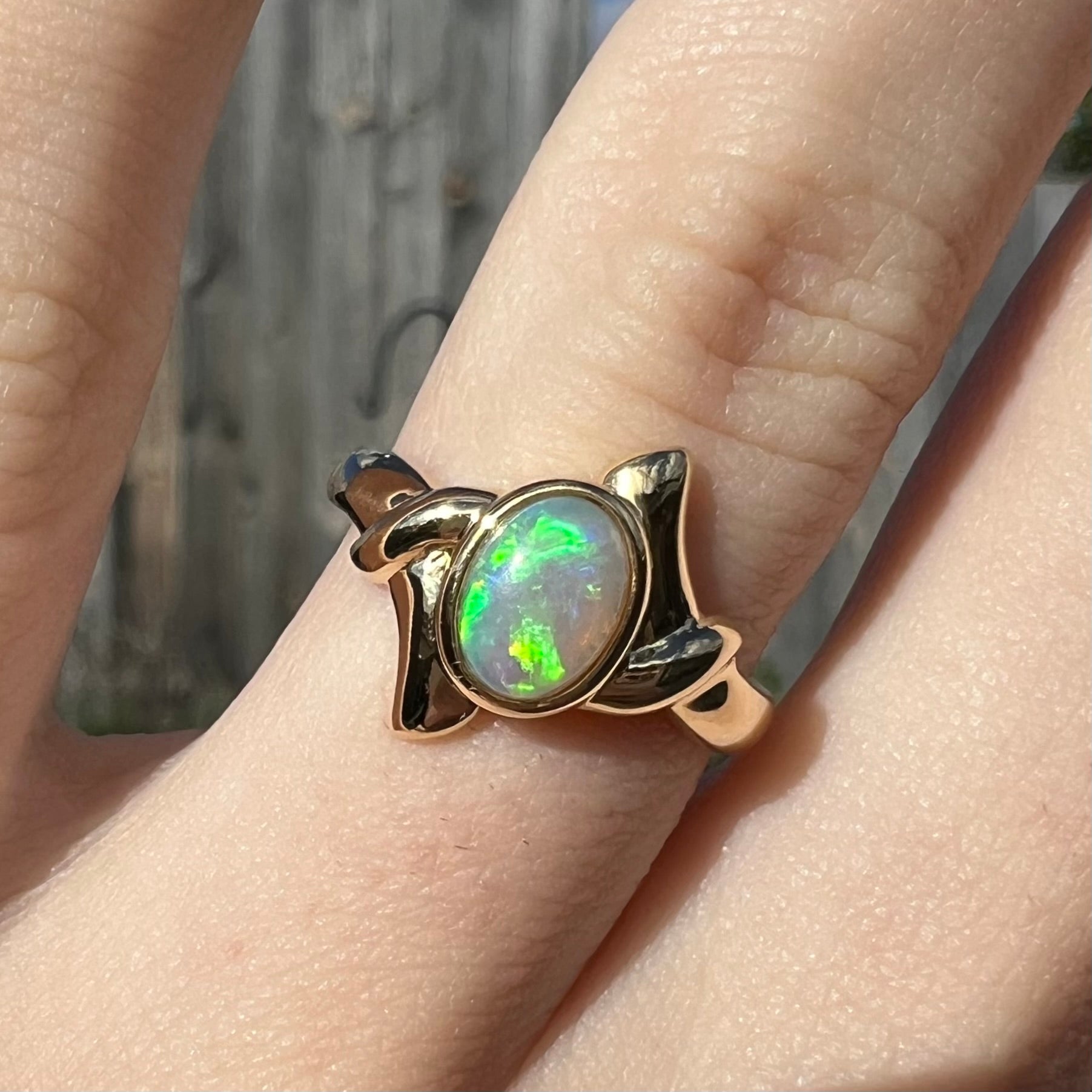 A dainty gold crystal opal ring worn on a hand.  The opal had vibrant green color play.