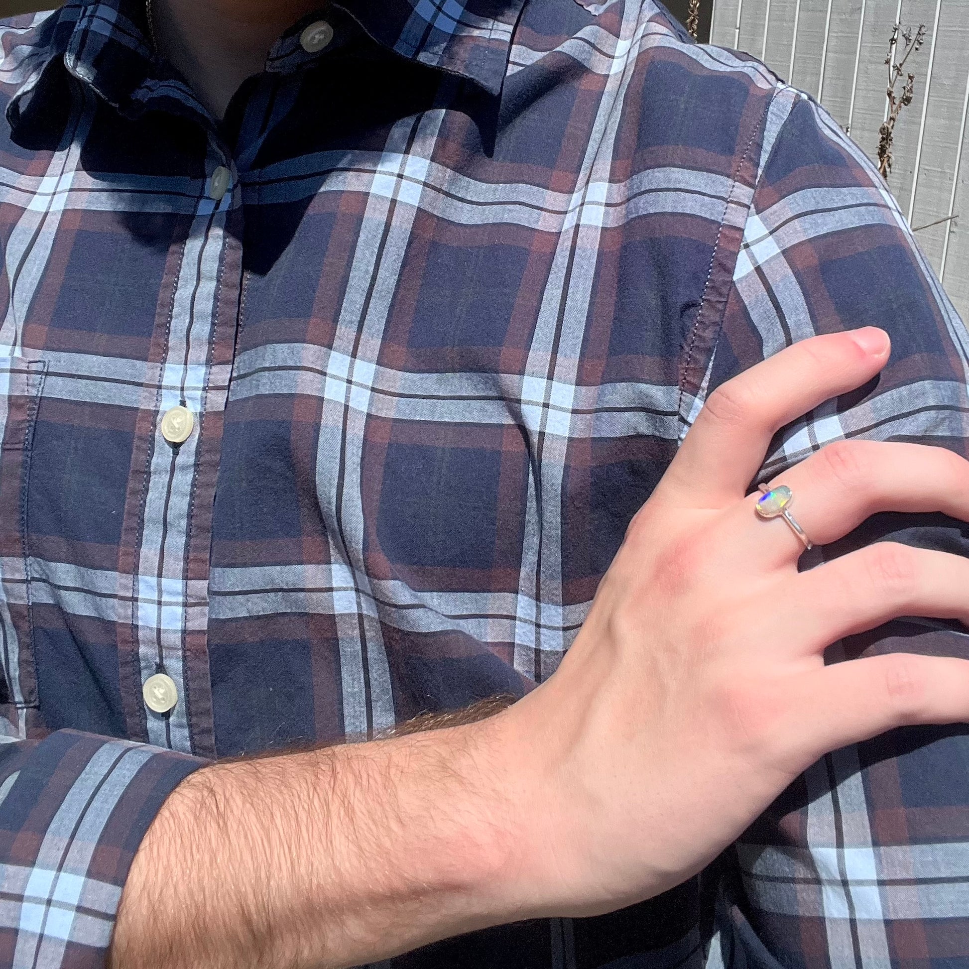 Person resting hand on their opposing shoulder in sunlight while wearing a dainty sterling silver crystal opal women's ring.
