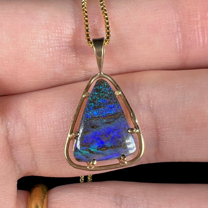 Close-up of a dainty Duck Creek opalized wood pendant in 9k gold, held in a hand.