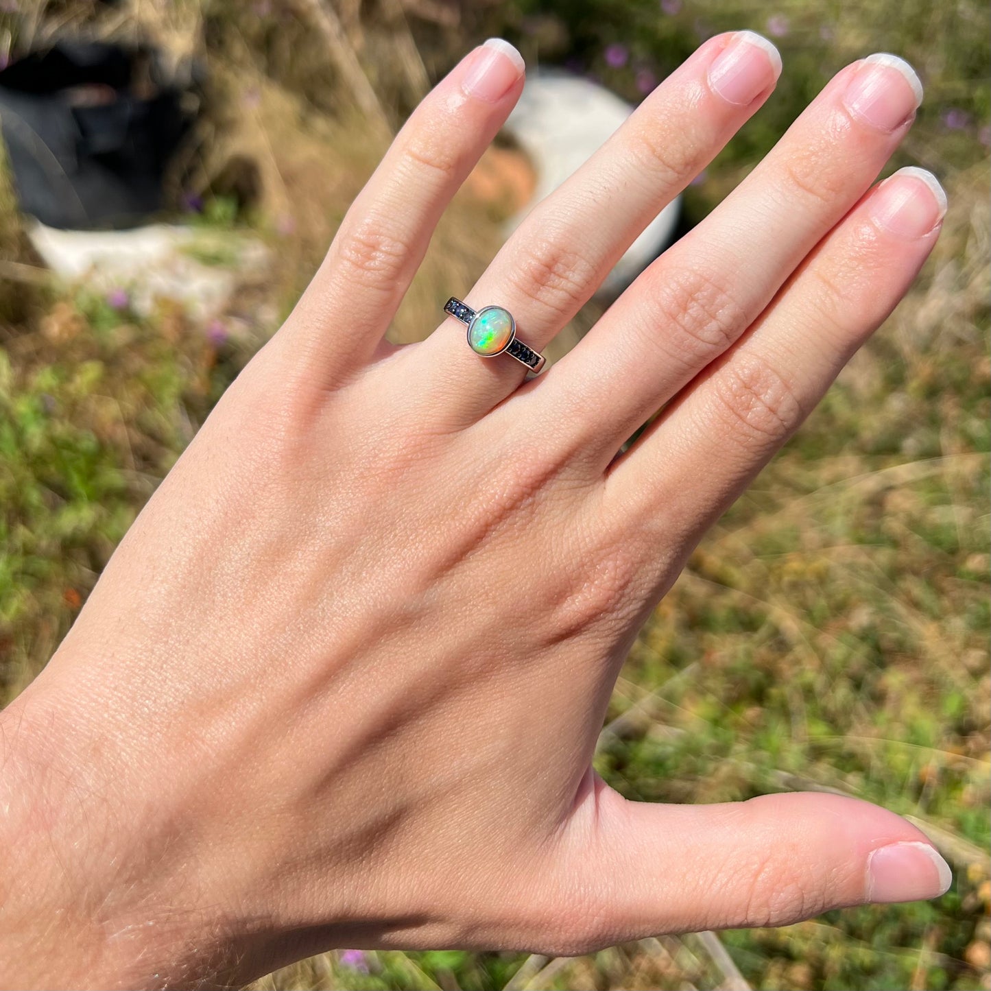 A dainty Ethiopian opal ring worn on a hand in the sunlight.  Subtle green fire is seen in the opal.