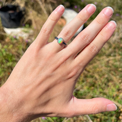 A dainty Ethiopian opal ring worn on a hand in the sunlight.  Subtle green fire is seen in the opal.