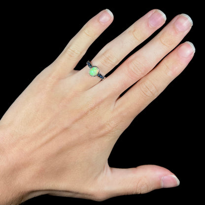 A dainty Ethiopian opal ring with channel set topaz accents worn on a hand against a black background.