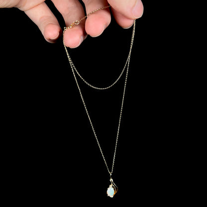 Dainty gold opal and diamond pendant suspended from 14k gold chain, dangled by hand