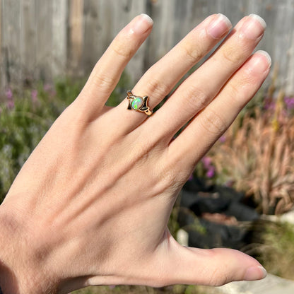 A dainty, 18k gold crystal opal engagement ring worn on a hand in the sunlight.