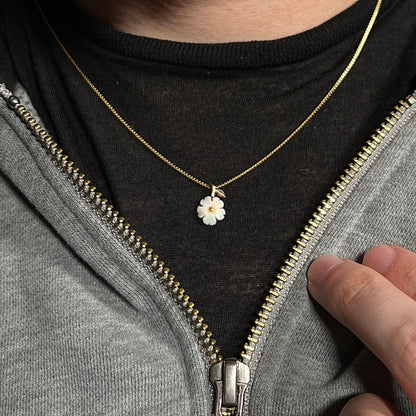 A dainty gold opal flower necklace shown worn around a person's neck against a dark shirt in a partially unzipped hoodie.