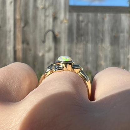 The gallery view of an 18k gold opal ring, worn on a finger in the sunlight.